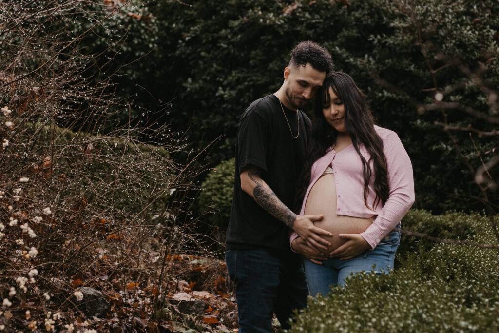 Lovely couple standing with foreheads together with husband's hands on pregnant belly.